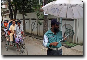 Dhaka street scene - umbrella'd police and bicycle rickshaws